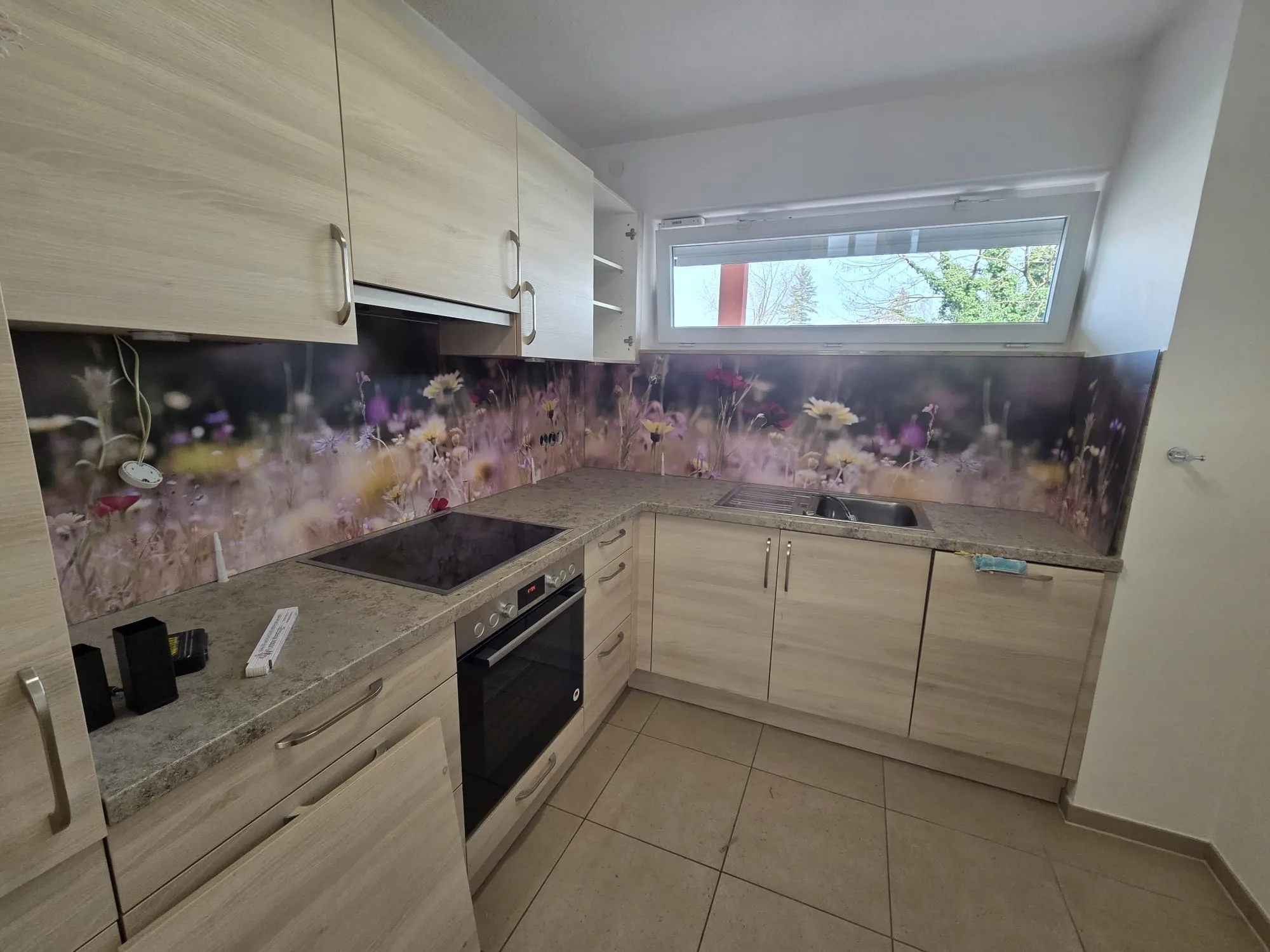 Helle Küche mit bedruckter Glasrückwand im Blumenwiesen-Motiv und Steinarbeitsplatte